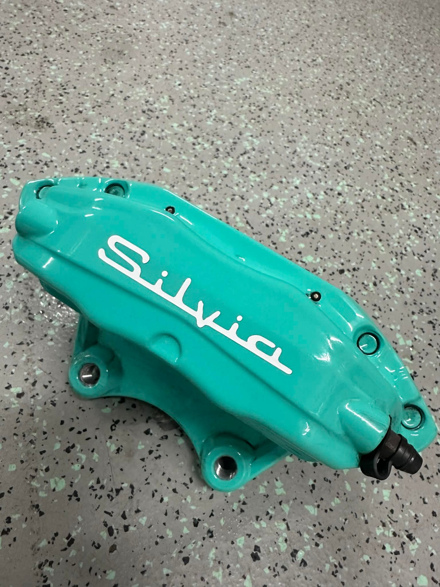 Turquoise brake caliper with 'Silvia' branding on a speckled gray surface